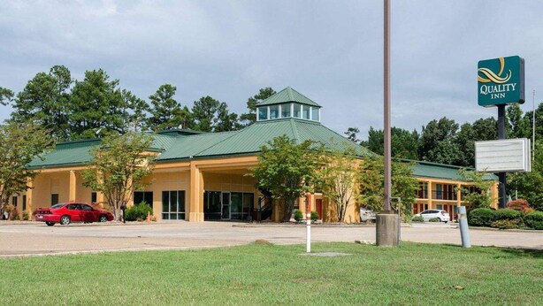 A hotel with a green roof, a signboard, and a red car parked in front. - Quality Inn Louisville MS (Louisville)