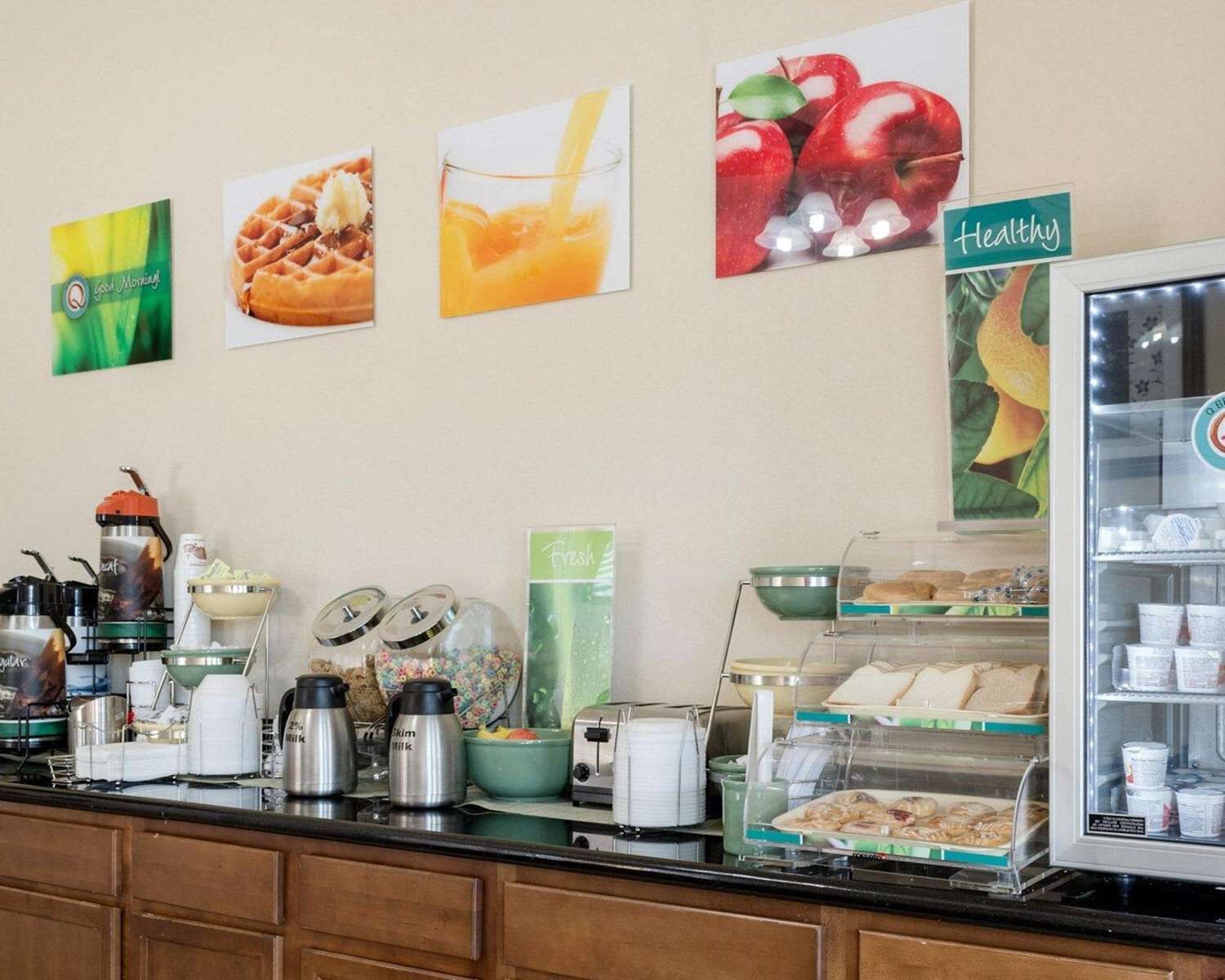 Un bufé de desayuno con diversas opciones de comida y salsas, una estación de café y un refrigerador con bebidas.