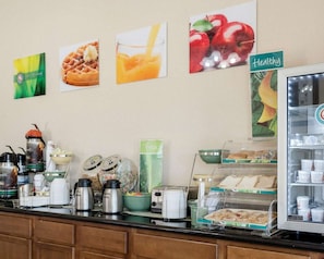 A breakfast buffet with various food items and condiments, a coffee station, and a refrigerator with beverages. - Quality Inn Louisville MS (Louisville)