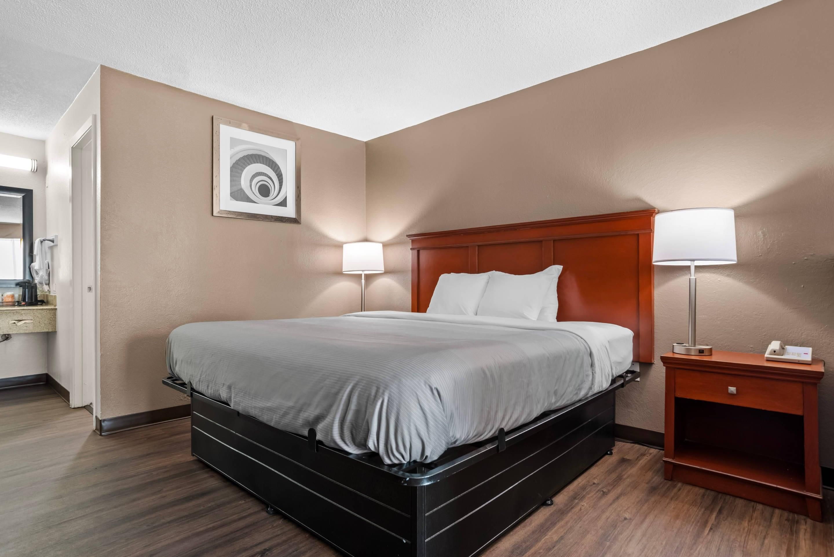 A hotel room with a bed, bedside lamps, a nightstand, a mirror, and a framed picture on the wall.
