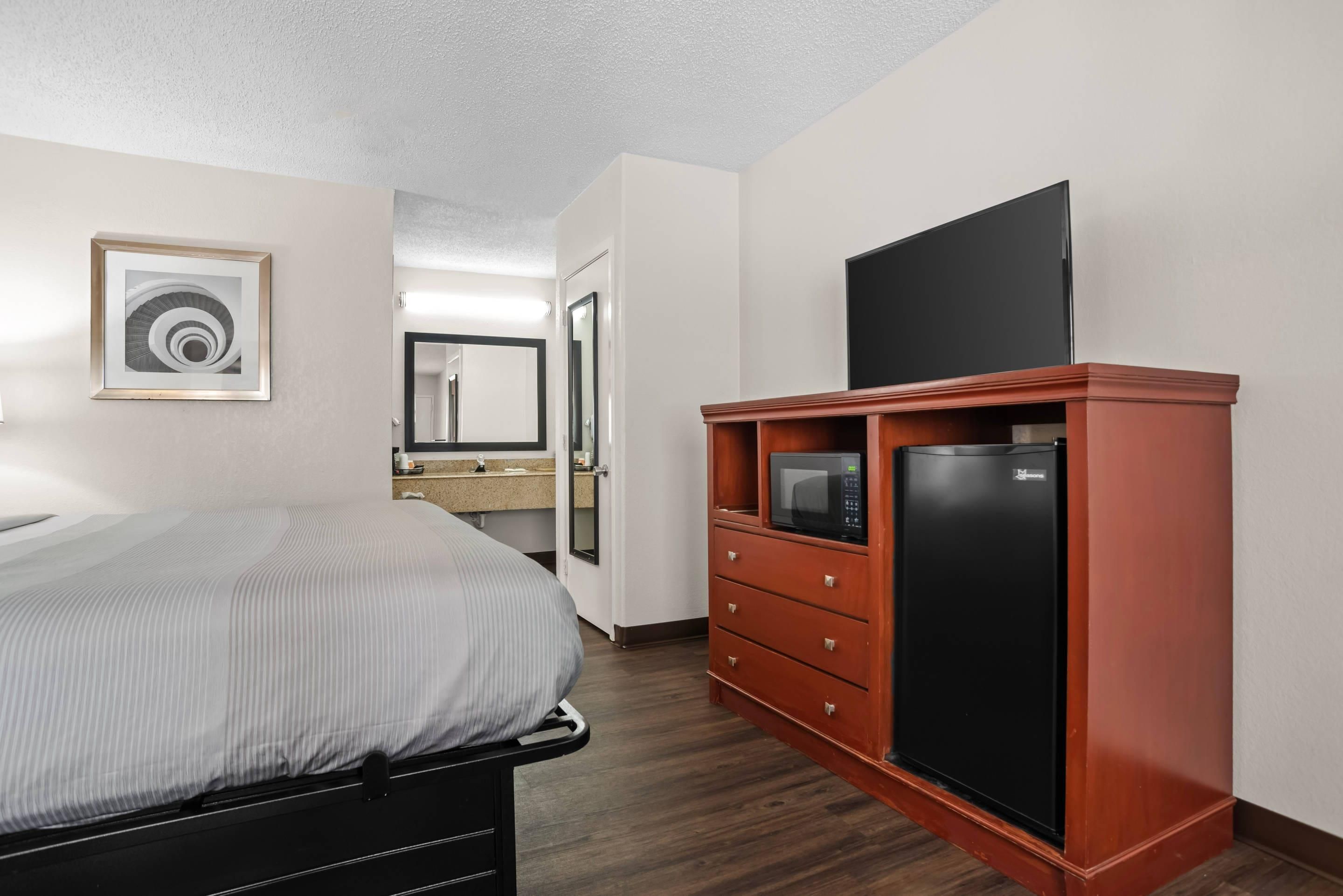A hotel room with a bed, a minibar, a television, and a bathroom visible through an open door.