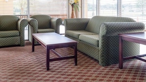 A room with a green patterned sofa, two armchairs, a wooden coffee table, and a patterned carpet. - Quality Inn Louisville MS (Louisville)