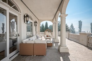 Un espace extérieur aménagé, abrité et doté de mobilier en osier, d’un fauteuil suspendu et offrant une vue sur les arbres et les montagnes.