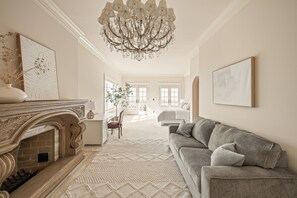 Un salon spacieux doté d’une cheminée, d’un lustre, d’un canapé et d’une grande fenêtre.