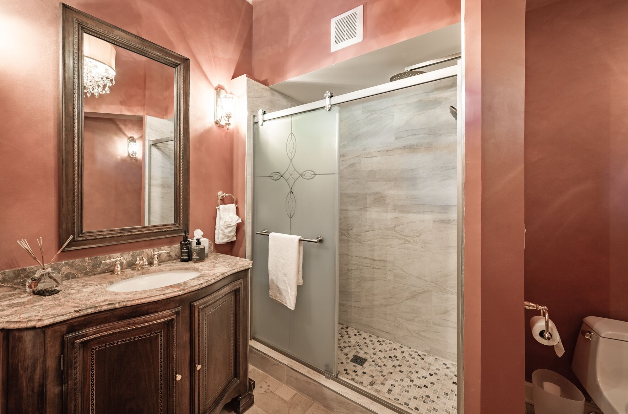 Une salle de bain avec un lavabo en marbre, un grand miroir, une cabine de douche en verre et des toilettes.