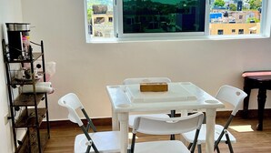 A room with a white table and chairs, a window with a view of buildings, and a shelf with items. - Hotel María Bonita Higüey,  room 301 Family property centrally located (Higüey)
