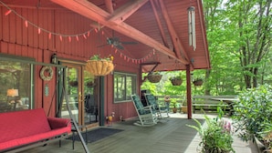 Una terraza de madera con un sofá rojo, mecedoras y macetas colgantes.