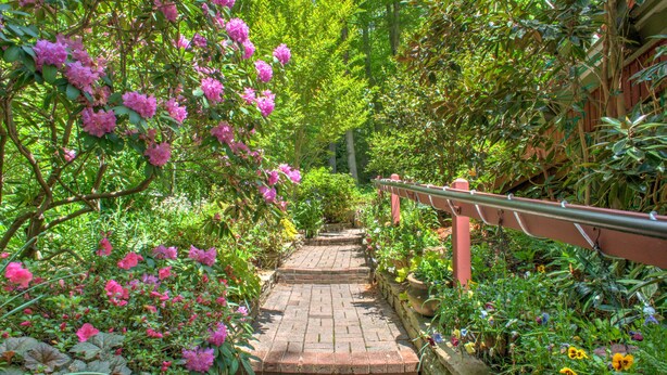 Un camino de ladrillo que atraviesa un jardín con flores rosadas y diversas plantas.