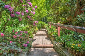 A brick pathway leading through a garden with blooming pink flowers and various plants.