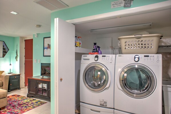 A laundry room with two stacked front-loading washing machines, a drying rack, and a colorful rug.