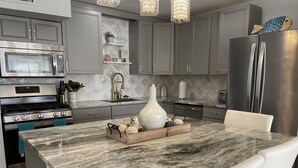 Une cuisine moderne dotée d’un îlot en marbre, d’appareils électroménagers en acier inoxydable et d’un vase décoratif.