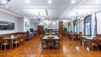 A spacious dining area with wooden flooring, multiple tables and chairs, and a large flat-screen TV mounted on the wall.