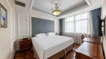 A hotel room with a large bed, a wooden desk, a television, and a window with curtains.