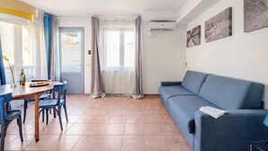 Ein modernes Wohnzimmer mit einem blauen Sofa, einem Esstisch mit Stühlen und einem großen Fenster mit Vorhängen.