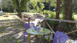 A rustic outdoor seating area with a round table and two purple chairs, surrounded by natural vegetation and a wooden fence.
