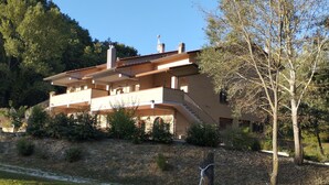 A large, multi-story building with a flat roof and multiple chimneys, surrounded by a grassy area and trees.