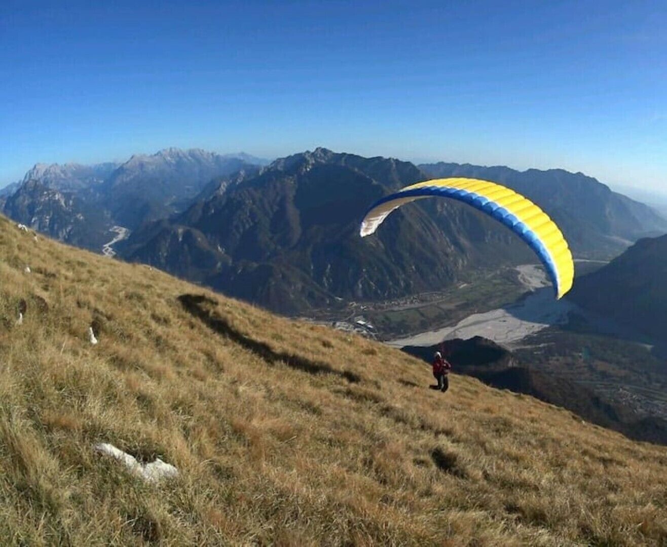 En person paraglider over et bjerglandskab med klare himmel.