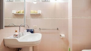 A bathroom with a white sink, a mirror, a toilet, and a green toilet brush.