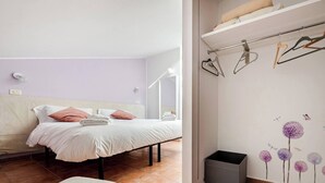 A bedroom with a bed, a chair, a wardrobe, and a trash bin.