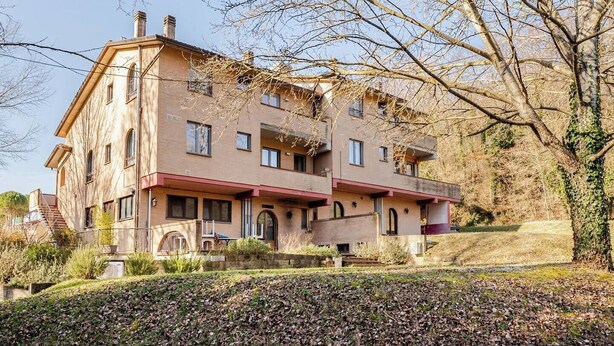 A multi-story building with a stone facade, multiple balconies, and a landscaped garden.