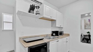 A modern kitchen with white cabinets, a dishwasher, a microwave, and a countertop with a sink. - Charming Studio Walking Distance To Ocean - Unit 8 (Hollywood)