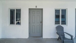 A house with a grey door, two windows with blinds, and a grey chair outside. - Charming Studio Walking Distance To Ocean - Unit 8 (Hollywood)