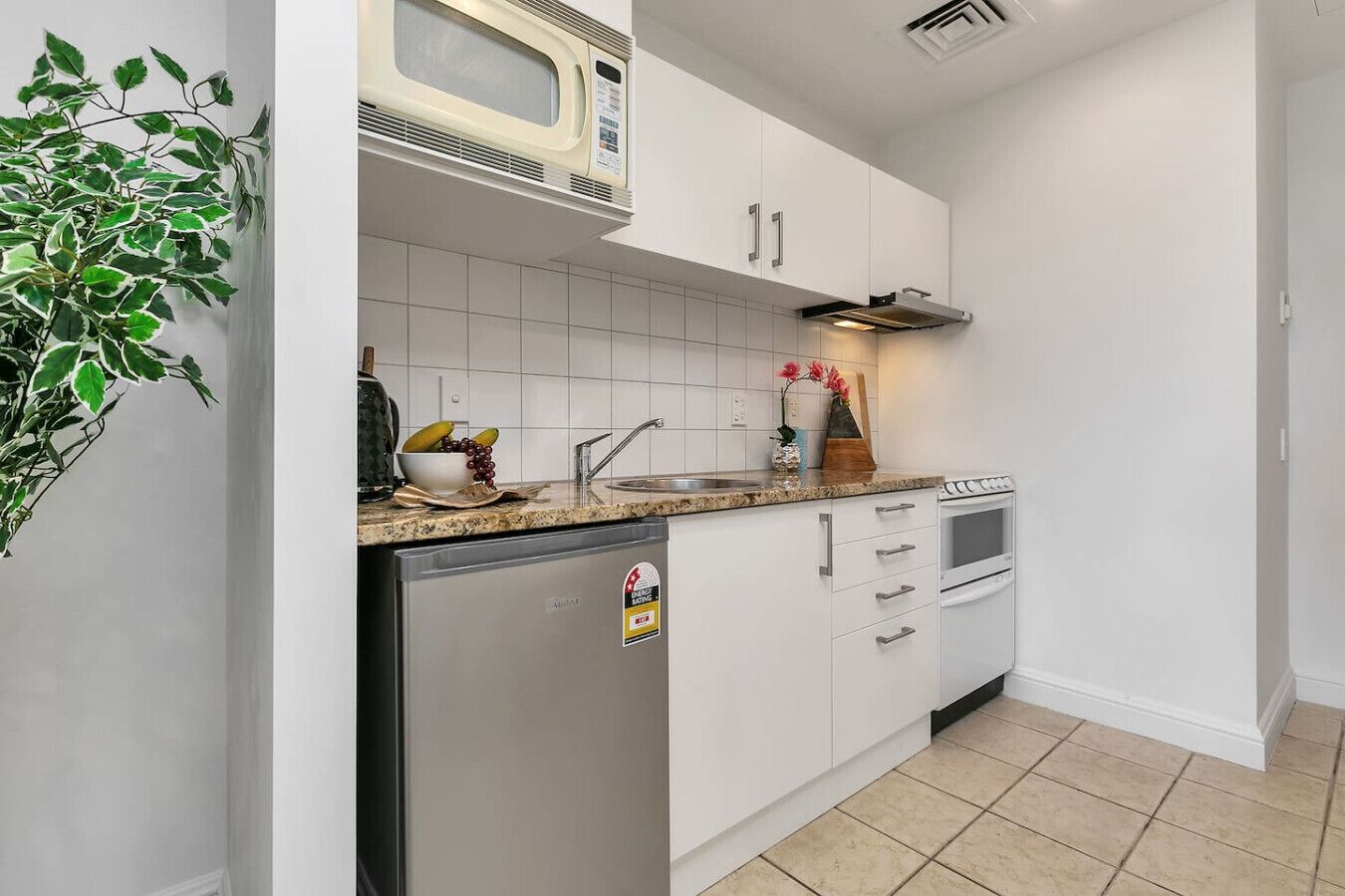 A compact kitchen with white cabinets, a built-in microwave, a sink, and a small refrigerator.