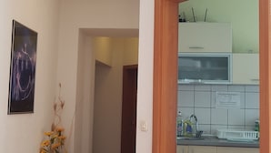 Un couloir menant à une cuisine équipée de meubles en bois, d’un banc et d’un tableau encadré accroché au mur.