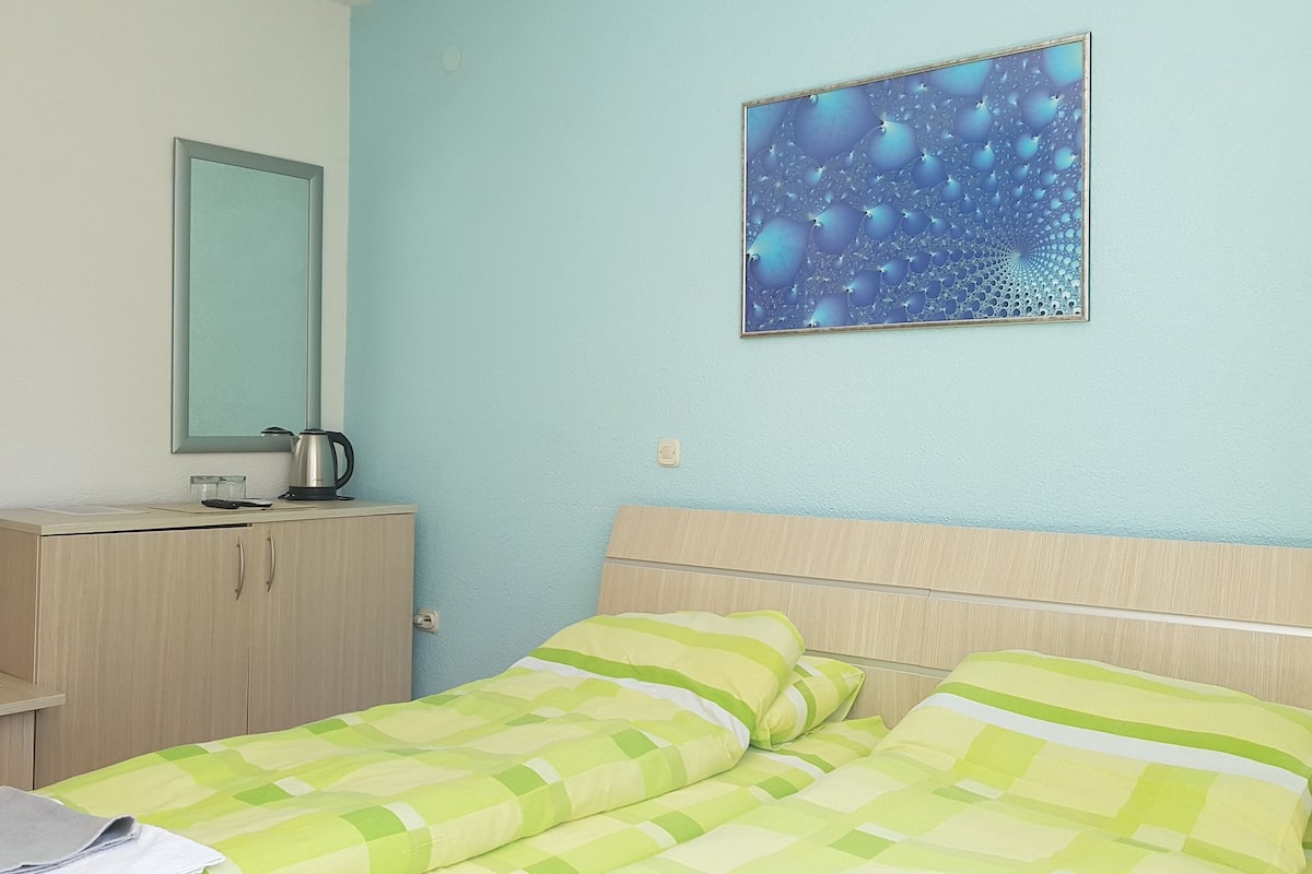 Une chambre avec un lit, une table de chevet avec une bouilloire, un miroir et un tableau accroché au mur.