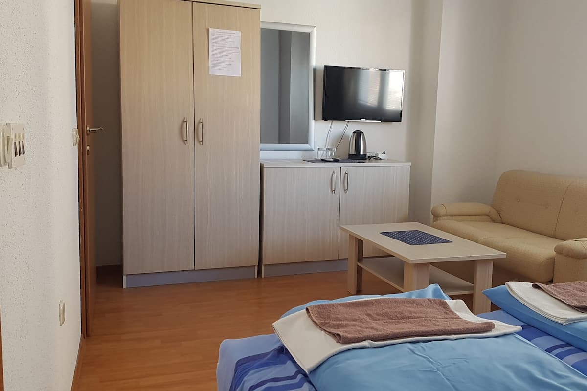 Une pièce de taille modeste comprenant un lit, une petite table, un canapé, un téléviseur et un coin cuisine.