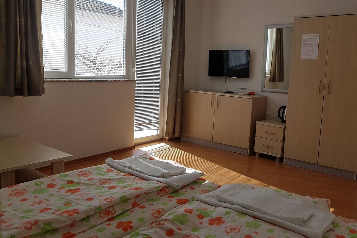 Une chambre d’hôtel équipée d’un lit, d’un bureau, d’une armoire, d’une télévision et d’une fenêtre avec des stores.