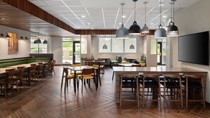Een ruime eethoek met houten tafels en stoelen, hanglampen en een grote flatscreen televisie aan de muur.