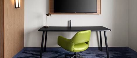 Una habitación con pared de madera, un escritorio negro, una silla de oficina verde, una lámpara negra y una pantalla negra grande montada en la pared.