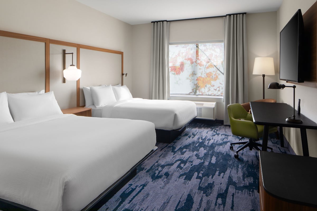 Een hotelkamer met twee bedden, een bureau, een stoel, een televisie en een raam met gordijnen.