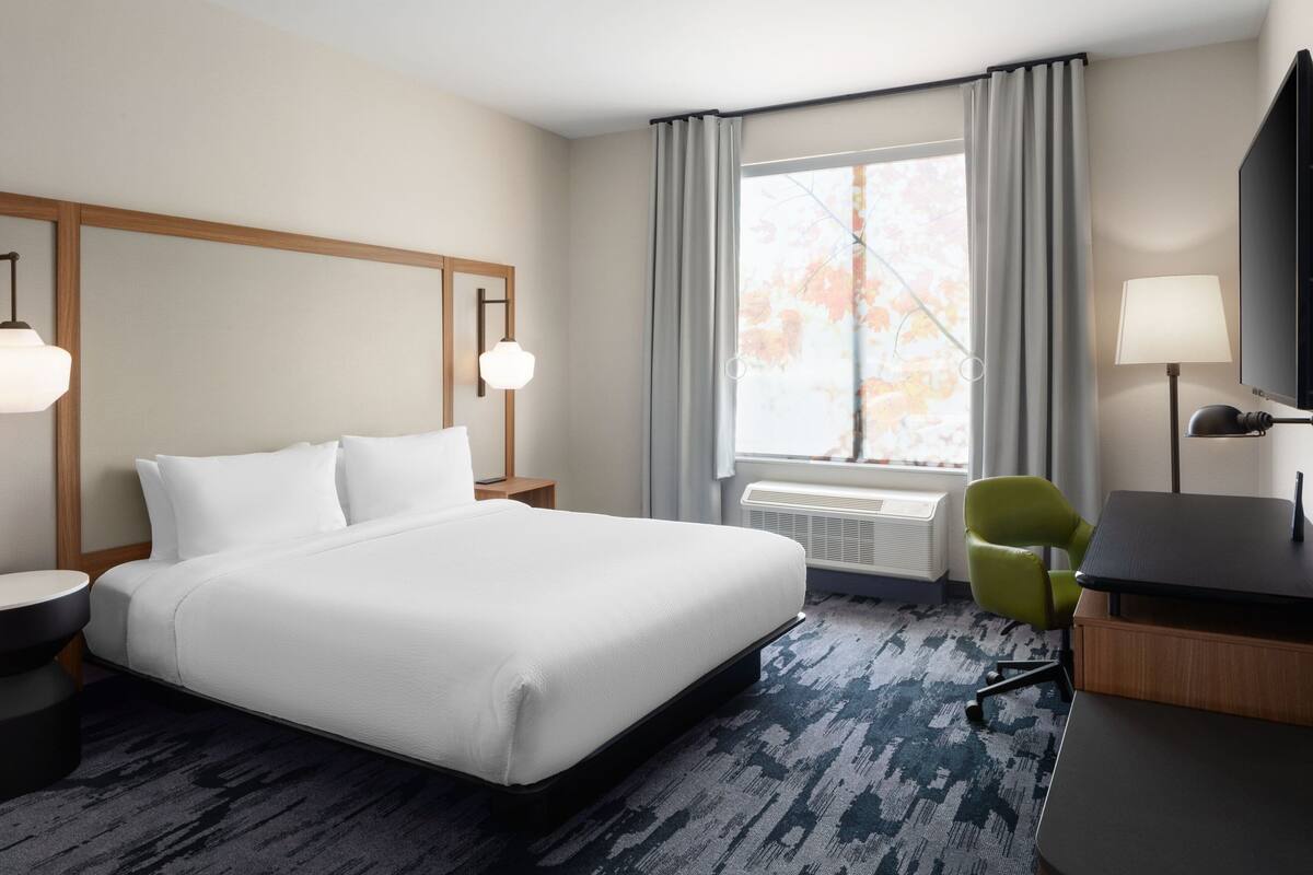 Een hotelkamer met een groot bed, een bureau met stoel, een televisie en een raam met gordijnen.