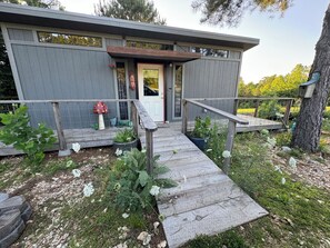 A modern house with a wooden deck, a front door, and a small garden area with plants and a mushroom decoration.