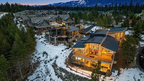 Un'ampia struttura ricettiva a più piani con un corpo centrale imponente, caratterizzato da ampie finestre e un balcone panoramico che lo abbraccia, circondata da edifici più piccoli e un paesaggio innevato con montagne sullo sfondo.