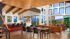 Un'ampia sala da pranzo con tavolo e sedie in legno, una cucina con dettagli rossi e ampie finestre che offrono vista sulle montagne.