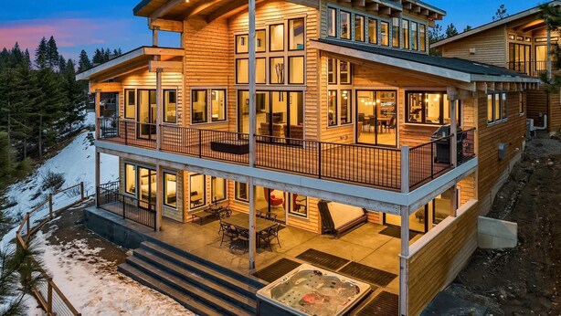 Una baita in legno a più piani con un balcone e una vasca idromassaggio al piano terra.