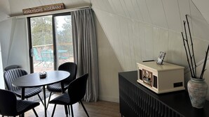 Un coin repas avec une table et des chaises, une enseigne indiquant « HONEYDOME HIDEAWAY », et une vue sur l’extérieur à travers une fenêtre munie de rideaux.