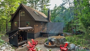 Une cabane avec un foyer extérieur, des sièges de jardin et un chemin en pierre.