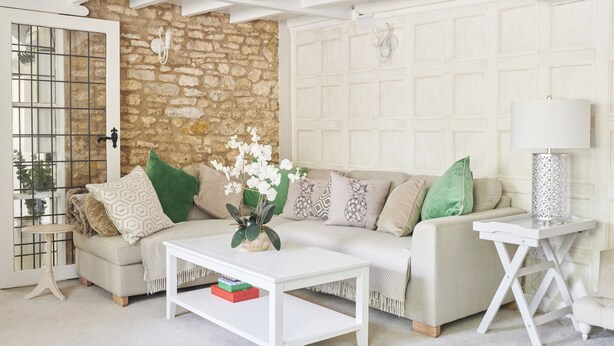 Un salon avec un mur en pierre, un canapé blanc, une table basse et une lampe.