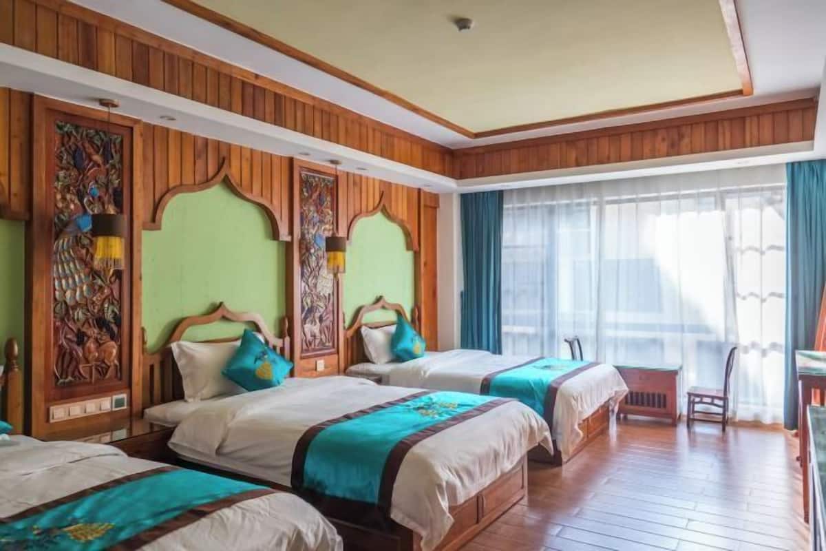 A hotel room with three beds, wooden paneling, and a large window with curtains.