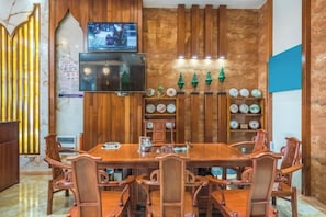 Un comedor con una mesa y sillas de madera, un televisor montado en la pared y estanterías decorativas.
