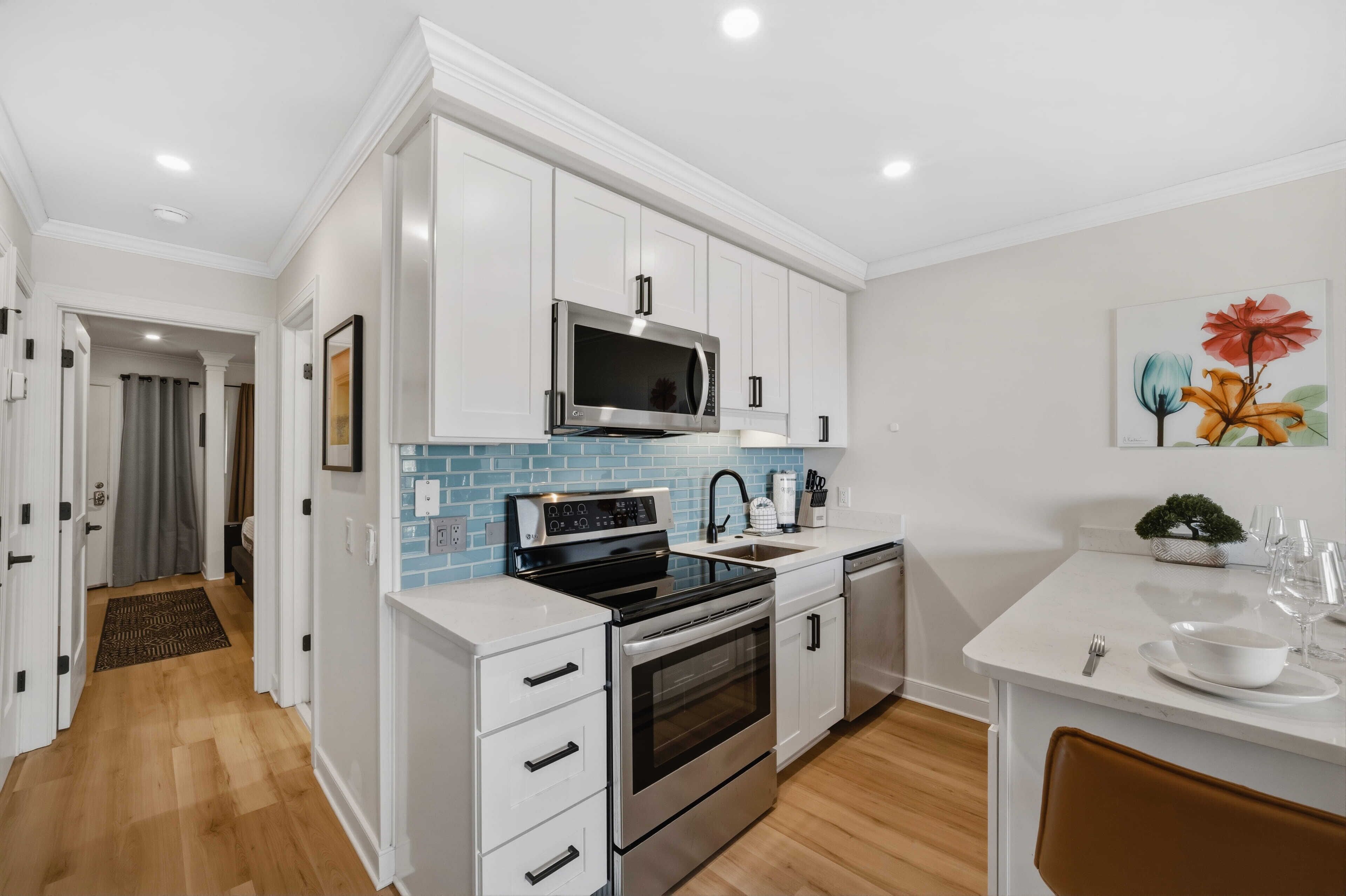 A modern kitchen with white cabinetry, stainless steel appliances, and a blue backsplash.