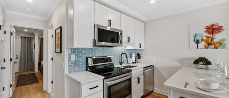 A modern kitchen with white cabinetry, stainless steel appliances, and a blue backsplash.