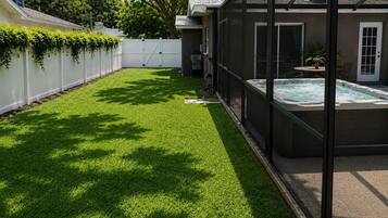 Ein Garten mit künstlichem Rasen, einem Whirlpool und einem weißen Zaun.