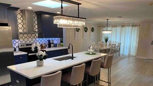 A modern kitchen with a central island, bar stools, and a dining area with a chandelier. -  HOT TOB HEATED POOL HOUSE, MINUTES FROM CLEARWATER BEACH (Clearwater)