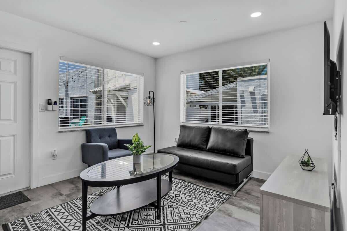 A modern living room with a glass coffee table, a dark sofa, and a TV on a stand.