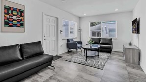 Un salon moderne avec un canapé en cuir noir, une table basse ronde et un tapis à motifs gris.